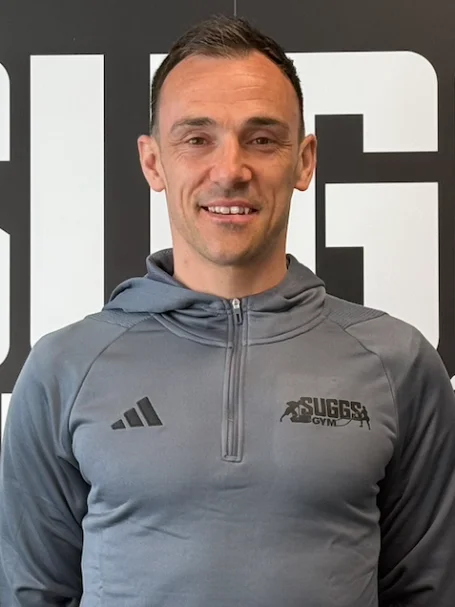 A coach in a Suggs Gym top, in front of the Suggs Gym sign